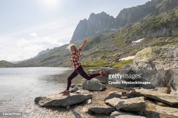 une randonneuse saute de rocher en rocher au-dessus d’un lac alpin - canton de graubünden photos et images de collection