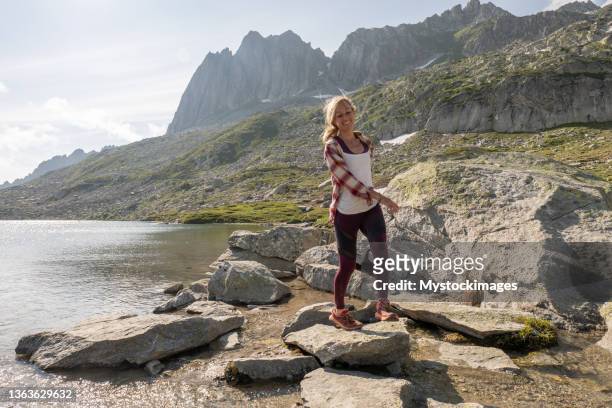 female hiker jumps from rock to rock above alpine lake - leap forward stock pictures, royalty-free photos & images