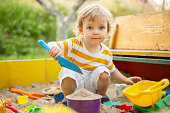 A little boy playing in the sandbox at the playground outdoors. Toddler playing with sand molds and making mudpies. Outdoor creative activities for kids