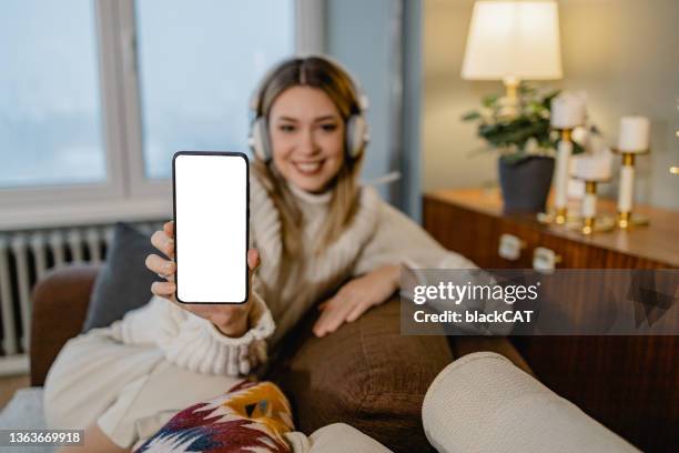 young woman holding mobile phone and shows empty screen - winter woman showing stock pictures, royalty-free photos & images