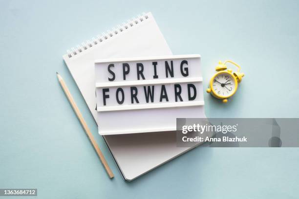 spring forward concept. alarm clock, pen and notepad. daylight saving time. - daylight saving time foto e immagini stock