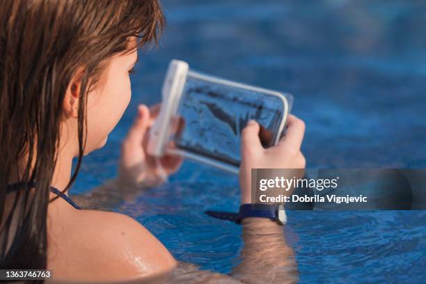 chica usando el teléfono en un recipiente de plástico en la piscina - impermeable fotografías e imágenes de stock