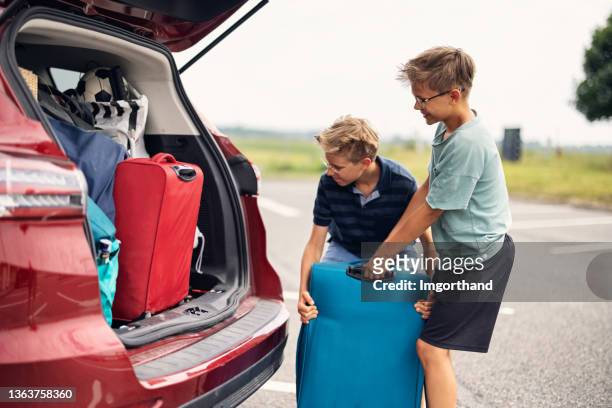 teenage boys helping to pack family car for road trip - carrying luggage stock pictures, royalty-free photos & images