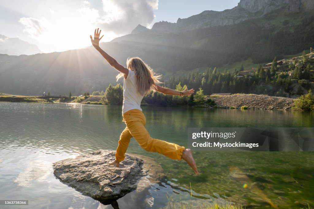 Wanderin springt von Fels zu Fels über Alpensee
