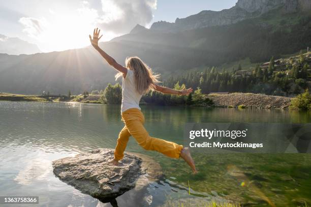 female hiker jumps from rock to rock above alpine lake - fitness woman jump stock pictures, royalty-free photos & images