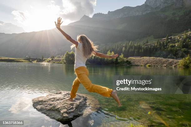 female hiker jumps from rock to rock above alpine lake - alpen sommer stock pictures, royalty-free photos & images