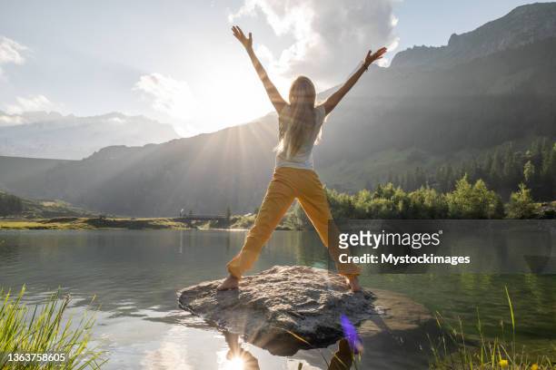 mujer joven se arma en la roca sobre el lago alpino al amanecer, feliz concepto de la mañana - letra x fotografías e imágenes de stock