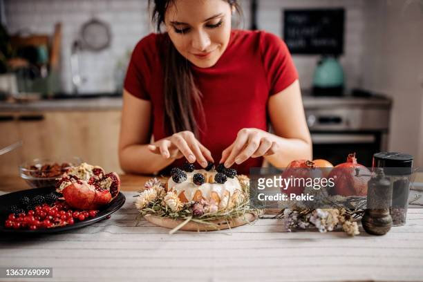 young beautiful woman decorating her cake with berry fruits - easter cake stock pictures, royalty-free photos & images