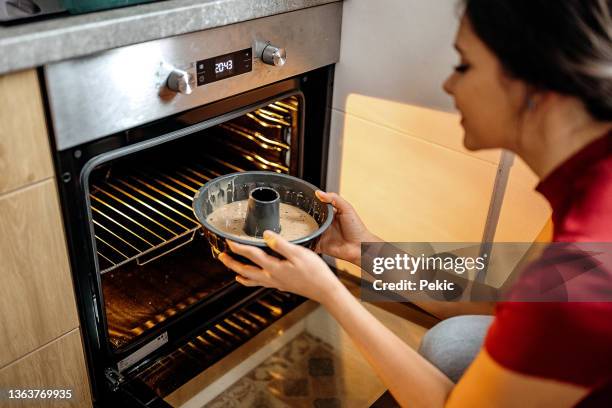 woman putting cake in oven - making cake stockfoto's en -beelden