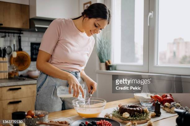 junge schöne frau, die in ihrer heimischen küche einen kuchen backt - schneebesen stock-fotos und bilder