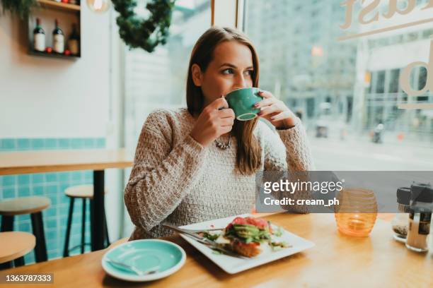 giovane donna che beve caffè e mangia toast all'avocado a colazione - lunch lady foto e immagini stock