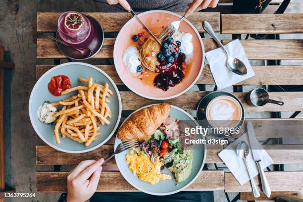 top view of friends having a good time enjoying english breakfast, blueberry pancake with a side of french fries in a cafe. people and food concept, eating out lifestyle - coppie cibo food bistrot foto e immagini stock