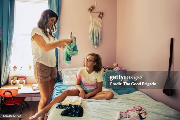 mother teaching daughter how to fold laundry in bedroom at home - middle class stock pictures, royalty-free photos & images