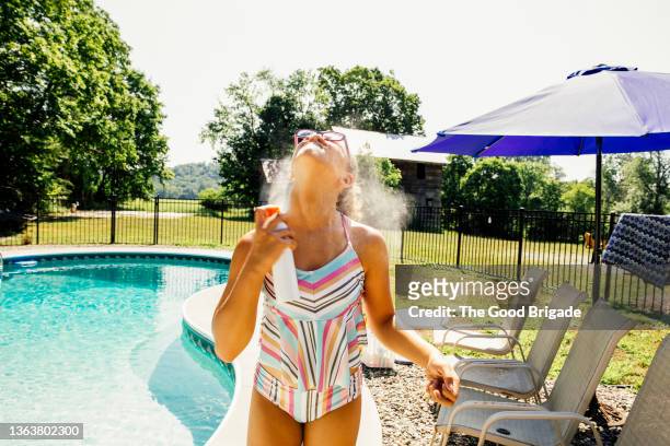 girl spraying sun protection on by swimming pool - tween girl swimsuit stockfoto's en -beelden