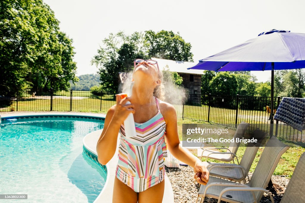 Girl spraying sun protection on by swimming pool