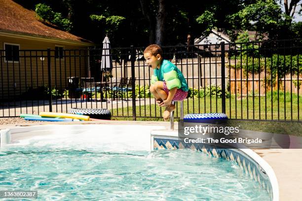 boy jumping into swimming pool on sunny day - arschbombe stock-fotos und bilder