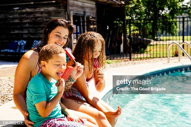 mother and children enjoying popsicles by swimming pool - eisstiel stock-fotos und bilder