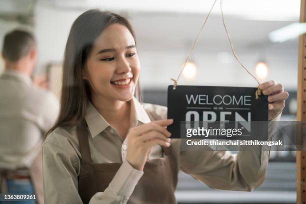 cropped shot of young woman hanging up an open sign of her coffee shop. - letrero de tienda fotografías e imágenes de stock