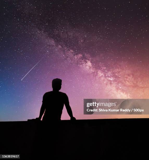 silhouette of man sitting on field against star field at night - sitting shiva stock pictures, royalty-free photos & images