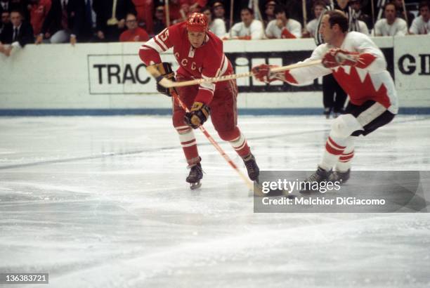 Alexander Yakushev of the Soviet Union skates with the puck as Bill White of Canada looks to hook him during the 1972 Summit Series at the Luzhniki...