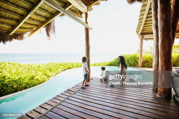 wide shot of smiling mother hanging out with son and friend by pool of luxury suite at tropical resort - family holidays hotel stockfoto's en -beelden