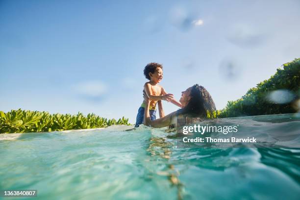wide shot of laughing mother and son playing in pool at tropical resort - wasser und spaß und erwachsene stock-fotos und bilder