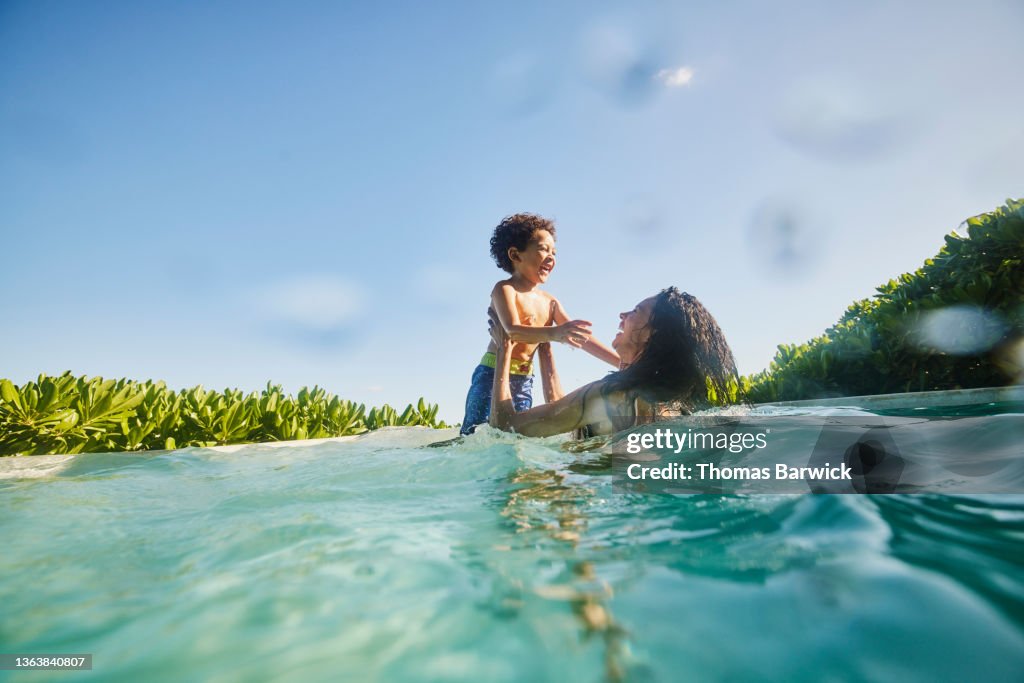 Wide shot of laughing mother and son playing in pool at tropical resort
