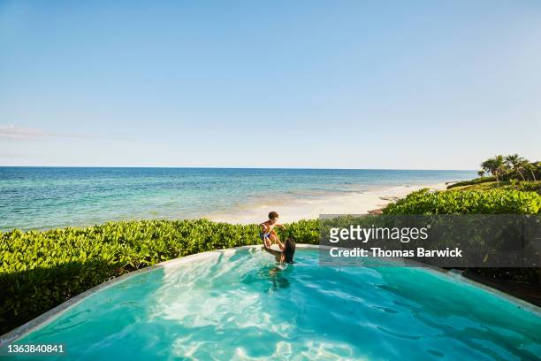 extreme wide shot of mother and son playing in pool of luxury suite overlooking beach at tropical resort - beach hotel imagens e fotografias de stock