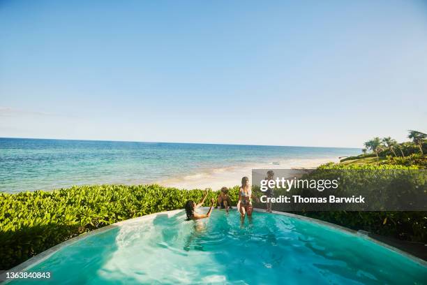 extreme wide shot of mothers and sons playing in pool of luxury suite overlooking beach at tropical resort - extreme wealth stock pictures, royalty-free photos & images