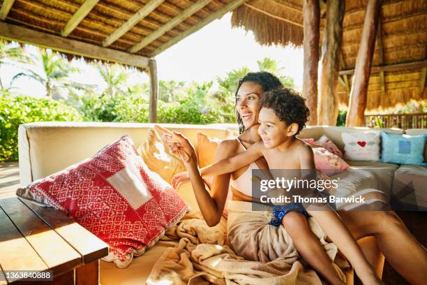 medium wide shot of smiling woman relaxing with son in outdoor lounge area of luxury suite at tropical resort - kids in undies stock-fotos und bilder