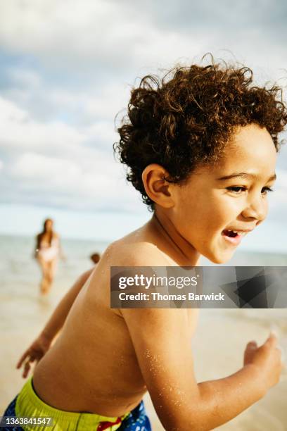 medium shot of smiling young boy running out of water while playing with mother on tropical beach - boy in swimwear stock-fotos und bilder