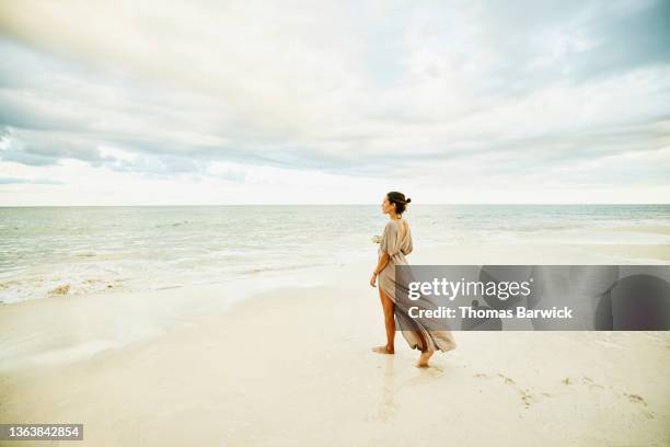 wide shot of woman walking on beach and enjoying sunset at tropical resort - beach photos et images de collection