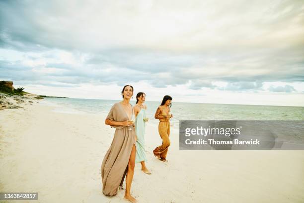 wide shot of female friends walking on beach at tropical resort at sunset - multi colored dress stock pictures, royalty-free photos & images