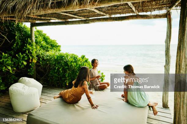 wide shot of female friends in discussion while relaxing in cabana on beach at tropical resort - belvedere stock pictures, royalty-free photos & images