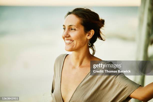 medium shot portrait of smiling woman hanging out on beach at tropical resort at sunset - traje beige fotografías e imágenes de stock