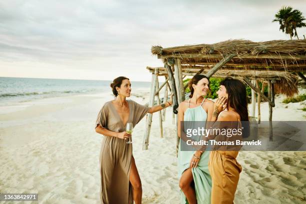 medium wide shot of female friends hanging out on beach at tropical resort at sunset - medium group of people foto e immagini stock