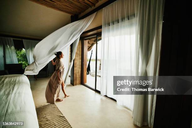 wide shot of woman standing in luxury hotel suite looking at view with curtains blowing in wind - hotel suite imagens e fotografias de stock