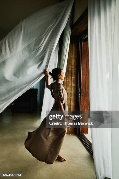 wide shot of woman standing by door of luxury hotel suite looking out at view with curtains blowing in wind - curtain blowing stock pictures, royalty-free photos & images
