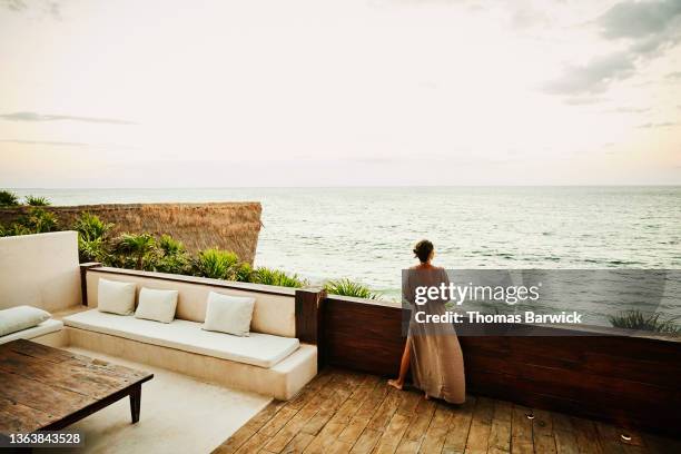 wide shot rear view of woman standing on deck of luxury hotel suite looking at ocean and sunset - ステータス ストックフォトと画像