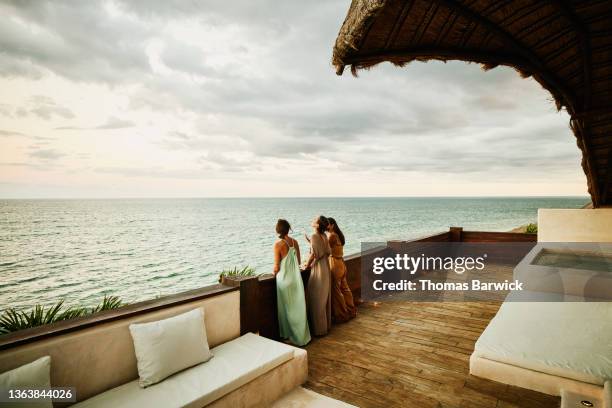 wide shot of laughing female friends standing on deck of luxury hotel suite looking at ocean and sunset - tropical elegance stock pictures, royalty-free photos & images