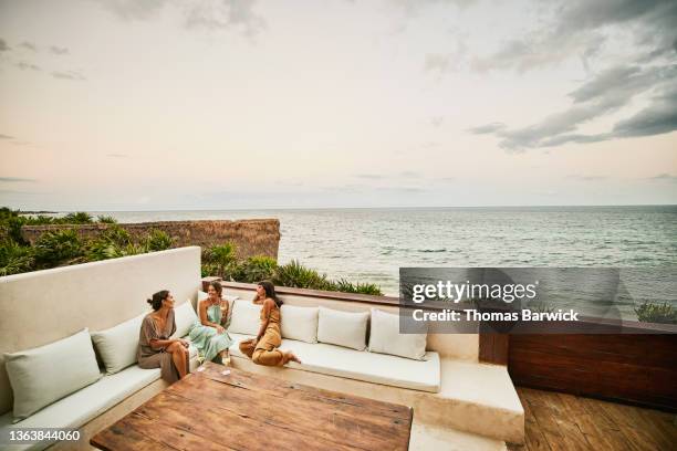 wide shot of smiling female friends relaxing on deck of luxury hotel suite at sunset - beautiful mexican women stock-fotos und bilder