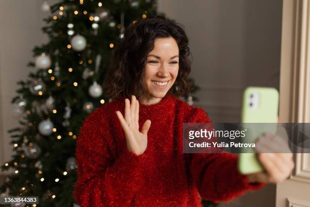 a woman communicates with her family, friends using a video phone on the background of a christmas tree - christmas family tree stock-fotos und bilder