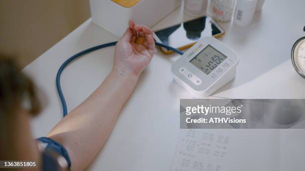 une femme âgée surveille la vérification de la pression artérielle en enregistrant ses chiffres de tension artérielle dans un ordinateur portable - blood pressure photos et images de collection