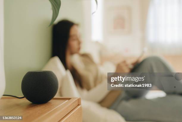 junge frau spricht mit sprachassistentin, um zu hause zu kontrollieren - smart speaker stock-fotos und bilder