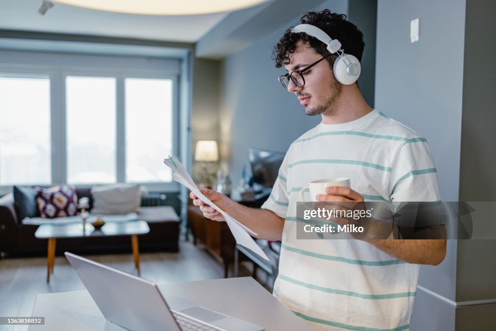 Young man at home using laptop and holding document