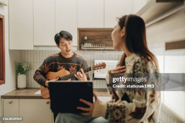 jeune couple chantant en s’amusant ensemble en cuisine. - party friends home guitar singers photos et images de collection