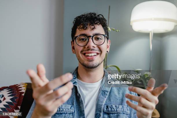 young man talking on a video call and looking at the camera - zwaaien gebaren stockfoto's en -beelden