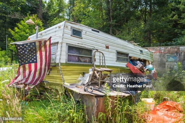 an old american flag hangs in front of an abandoned mobile home in rural america. - trailer trash stock pictures, royalty-free photos & images
