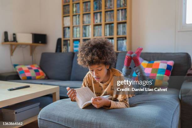 african- american boy reading a book on the sofa - kids read fotografías e imágenes de stock