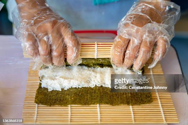 close up of hands rolling up a sushi with a bamboo mat - sushi rice stock pictures, royalty-free photos & images